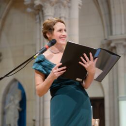Chanteuse d’opéra se produisant lors d’un concert de Noël dans une église, vue de profil, souriante, cheveux attachés, elle porte une robe verte